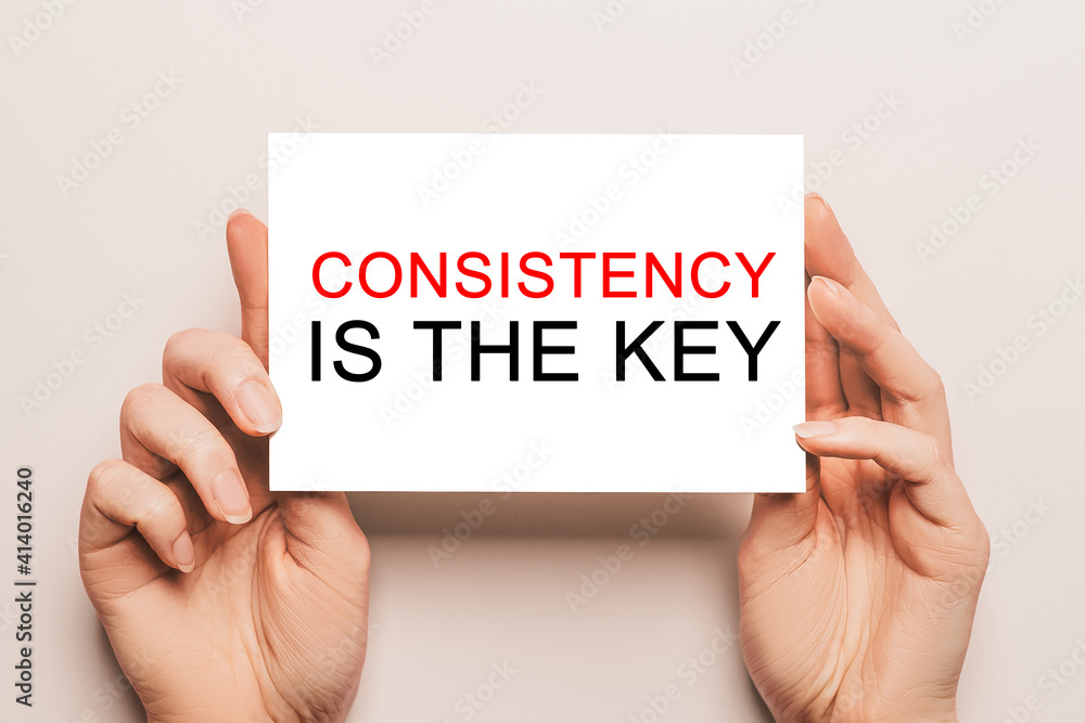 Female hands hold card paper with text Consistency is the key on a yellow background. Business and finance concept Female hands hold card paper with text Consistency is the key on a yellow background. Business and finance concept