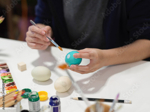 Female hands painting Easter eggs with poster colour and other paint tools