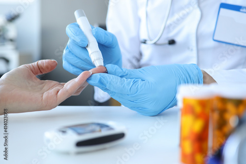 Doctor piercing patients finger with lancet in clinic closeup photo