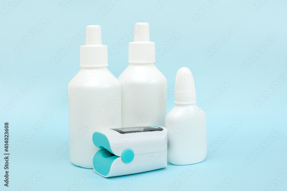 White plastic bottles of medicines and pulse oximeter on blue background White plastic bottles of medicines and pulse oximeter on blue background