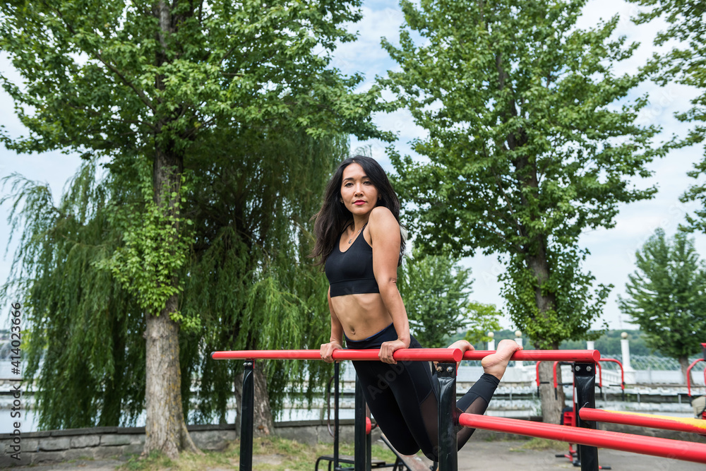 Naklejka premium Beautiful sexy woman makes exercise on horizontal bar sunny day for perfect street workout