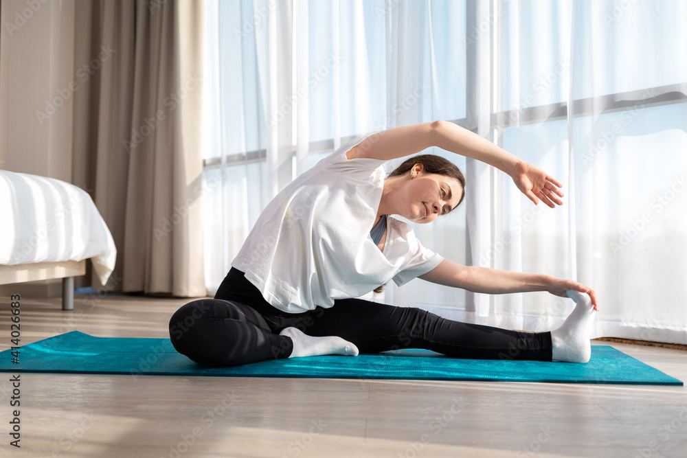 Naklejka premium A young pretty woman in sportswear doing yoga on the sports mat. Indoors. The concept of sports at home