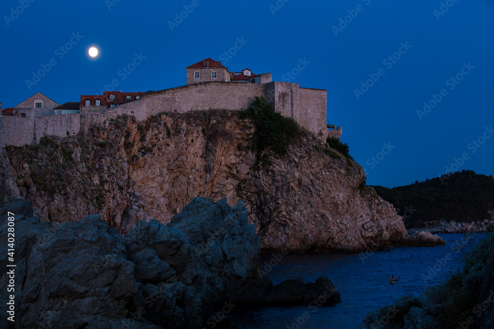 .Night Photograph of City of Dubrovniks Walls on a Cliff with a Full Moon and Sea in the background.