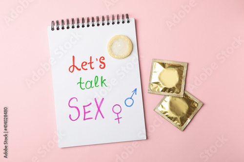 Notebook with Let's talk Sex and condoms on pink background photo