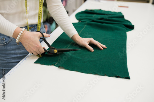 Closeup of seller cutting fabrics in textile store. Seamstress using scissors to trim the material on work table. Small Business Concept
