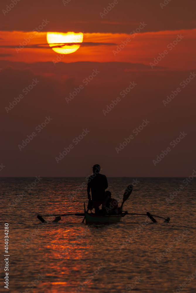 Silhouette of a fisherman on board a boat against the golden hour of sunset