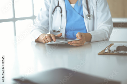 Unknown woman-doctor standing in clinic and using tablet pc  close-up. Data and best service in medicine and healthcare