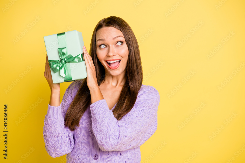 Portrait of lovely amazed cheerful girl holding in hands giftbox guessing what's inside isolated over bright yellow color background Portrait of lovely amazed cheerful girl holding in hands giftbox guessing what's inside isolated over bright yellow color background