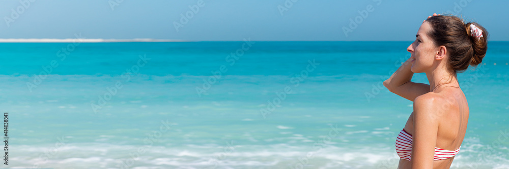 Young woman in a swimsuit against the background of the sea and blue sky. Banner.