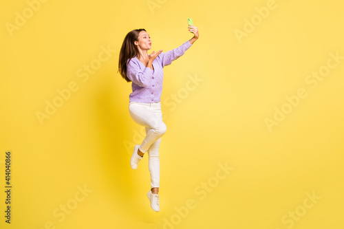 Full length body size view of lovely funky fit girl jumping taking selfie sending air kiss isolated over bright yellow color background