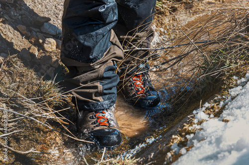 Waterproof boots for hiking, shoes in the water. Detail of men's climbing boots walking through watery footpath in the mountains photo