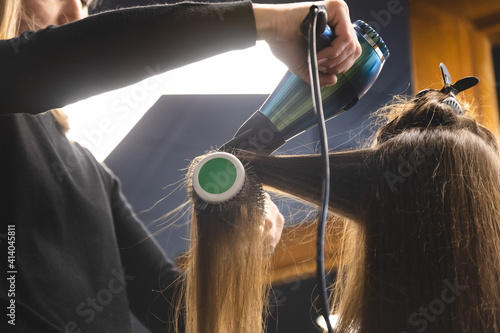 Master woman hairdresser dries the girl's hair with a hairdryer and combs after washing in the beauty salon