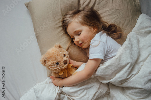 Little girl sleeping in bed embracing soft toy at home, top view
