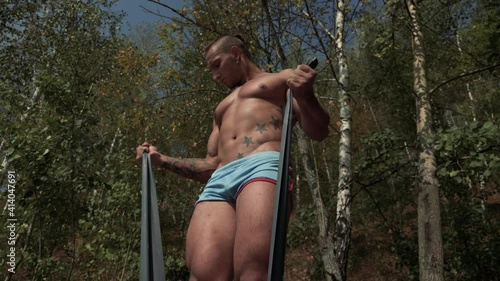 Tattooed bodybuilder with an earring in one ear pumps his hands with a fitness elastic band