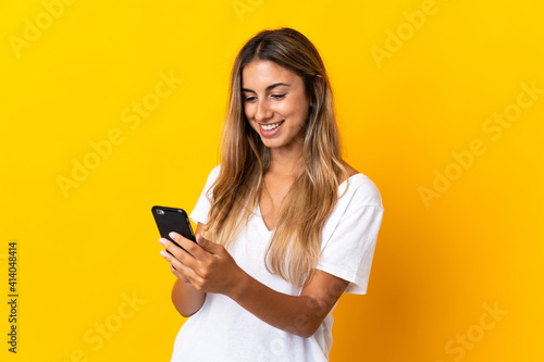 Young hispanic woman over isolated yellow background sending a message or email with the mobile