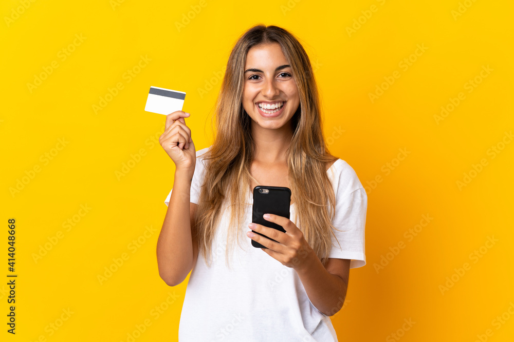 Young hispanic woman over isolated yellow background buying with the mobile with a credit card Young hispanic woman over isolated yellow background buying with the mobile with a credit card