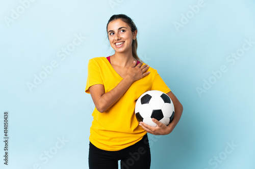Young hispanic football player woman over isolated on blue background looking up while smiling © luismolinero