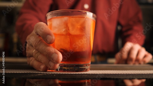 Bartender serves a Negroni cocktail on the bar counter.