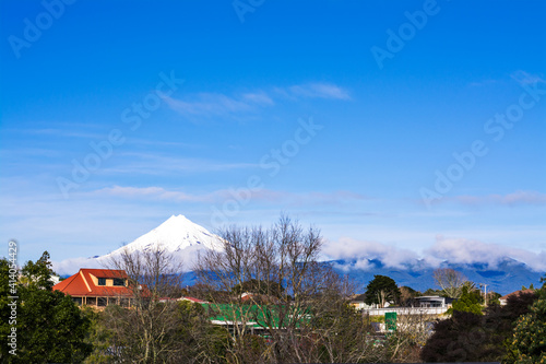 Snow covered cone of Mount Taranaki is clearly visible behind city suburb. New Zealand © Irina B