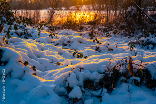Sonnenuntergang beleuchtet den Schnee vor dem See mit dem Schilf