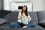 beautiful woman sitting on a sofa with bent legs pillow in hands Comfort in an apartment