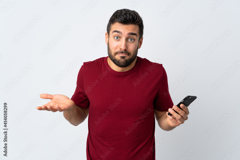 Young handsome man with beard using mobile phone isolated on white background making doubts gesture while lifting the shoulders Young handsome man with beard using mobile phone isolated on white background making doubts gesture while lifting the shoulders