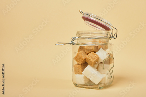 Fotografie brown and white sugar cubes in a jar with a sealed lid, beige background