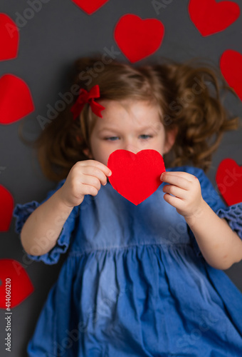 Top view of a happy little girl in a blue dress. The girl holds a red paper heart in front of her. The concept of Valentine's Day, March 8, Mother's Day, Father's Day.