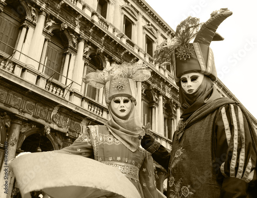 Noble couple masks in costumes decorated with flowers, butterflies and birds at St Mark's Square during traditional Carnival.  Venice, Italy. Nature and environment theme. Sepia historic photo. photo