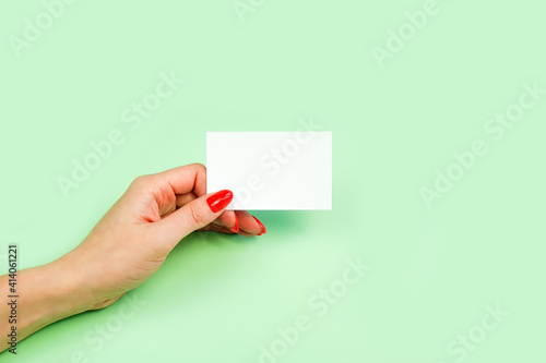 Female hand with red manicure holding blank white business card, close-up, isolated on green background