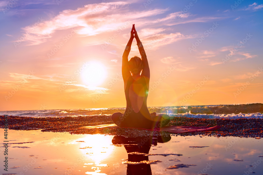Woman practicing yoga on the beach at sunset or sunrise. Meditation.