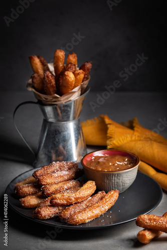A plate with churros - fried dough, with dulce de leche, slowly heating sweetened condensed milk. Dark background, vertical image.