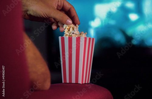Eating popcorn while watching a movie on the couch at home. Scene in a house with bright lights  a movie night with the scent of pop corn.