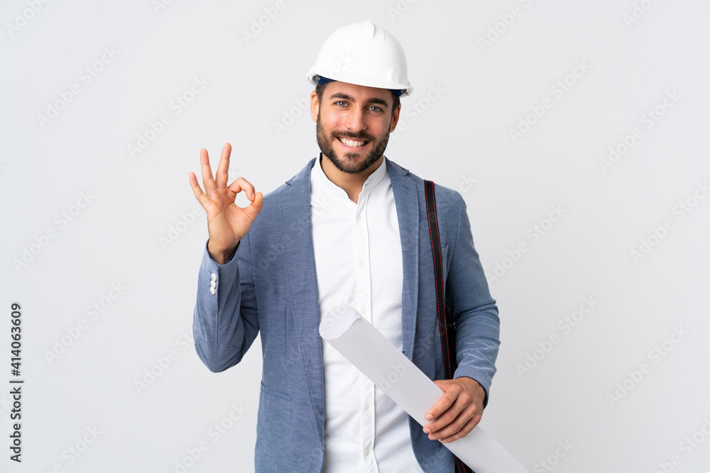 Young architect man with helmet and holding blueprints isolated on white background showing ok sign with two hands Young architect man with helmet and holding blueprints isolated on white background showing ok sign with two hands