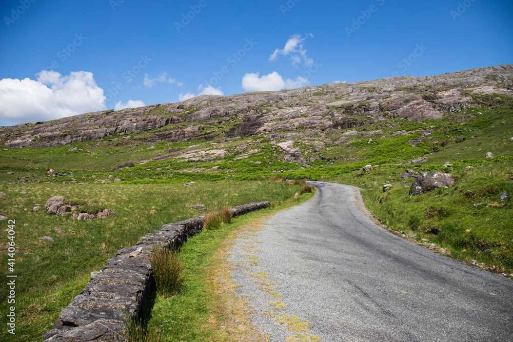 Fototapeta premium A remote and empty country side Irish road in county Kerry, with green fields and distant mountains in the background