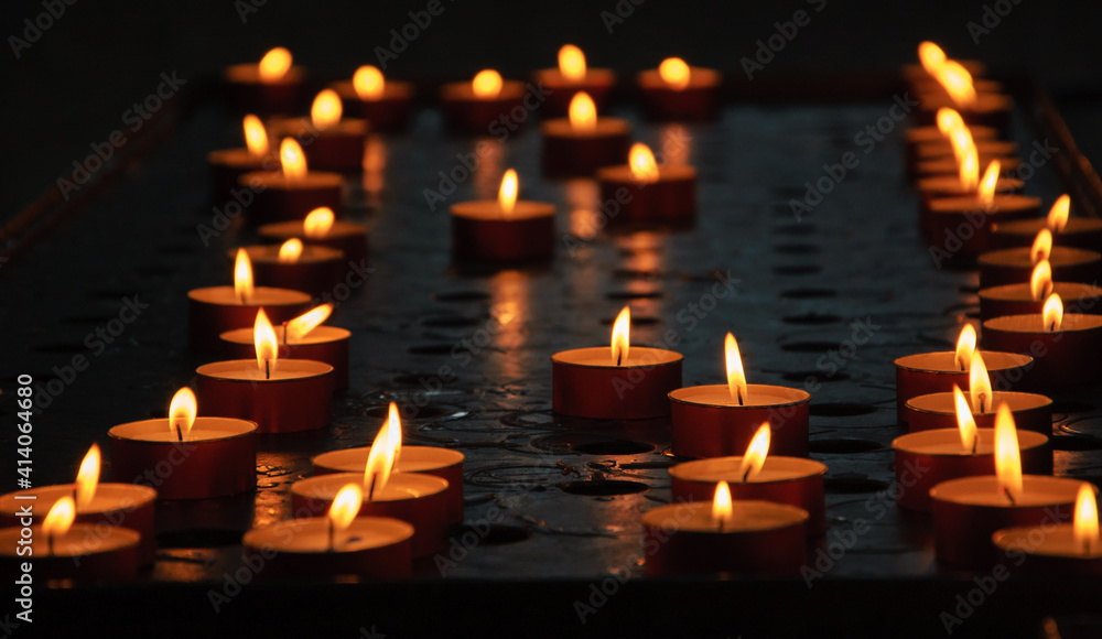 Burning candles in dark church. Golden flame glow. Reflection. Religious background.