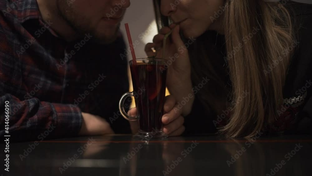 A young, beautiful couple is drinking a cocktail in the evening in a restaurant against the backdrop of the night city in the window. A young, beautiful couple is drinking a cocktail in the evening in a restaurant against the backdrop of the night city in the window.