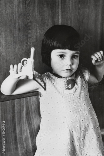 Portrait of little soviet girl with toy gun in hand, black and white. Early 1980s. Old surface, soft focus. Transferred property, family archive.