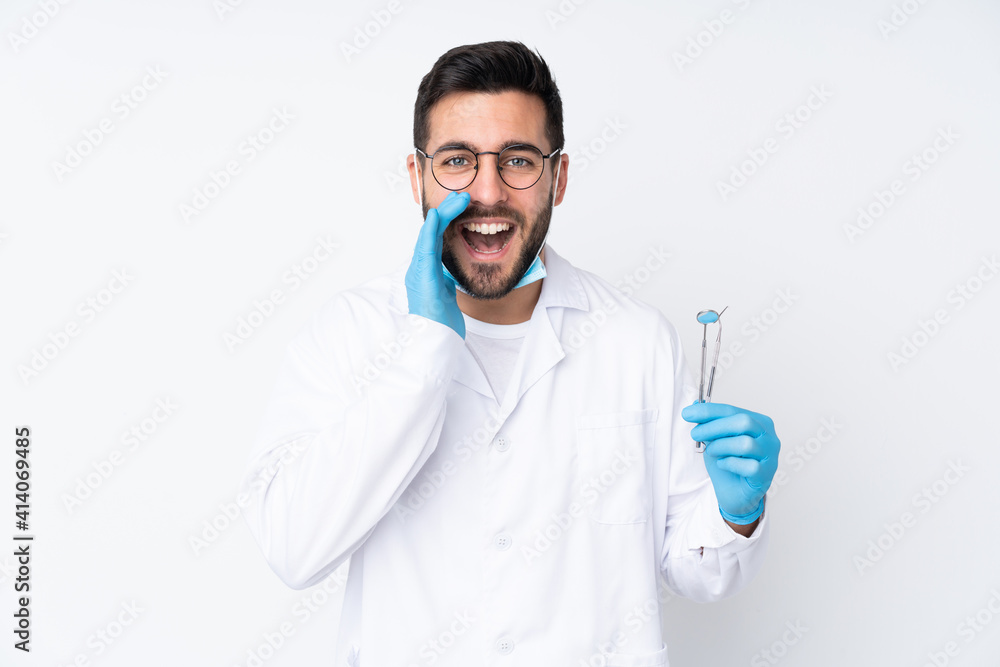 Dentist man holding tools isolated on white background shouting with mouth wide open Dentist man holding tools isolated on white background shouting with mouth wide open