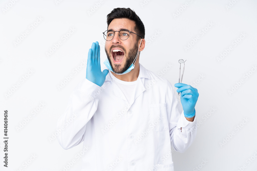 Dentist man holding tools isolated on white background shouting with mouth wide open