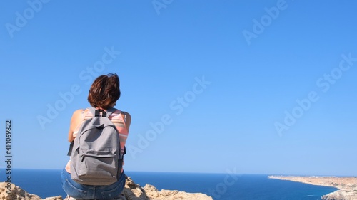 Girl tourist with a backpack on the background of the sky, back view