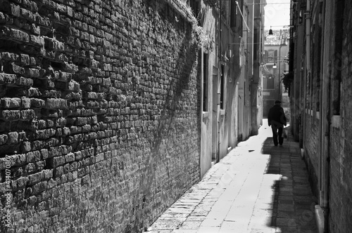 Silhouette of  old man going on narrow street in shining sun rays. Venice  Italy. A game of light and shadow. Black white historic photo.