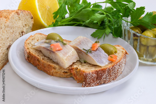 Open sandwich with pickled herring slices and olives, close-up