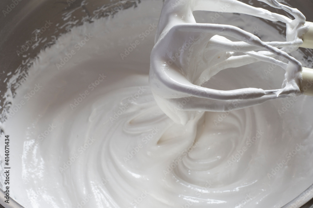 Egg whites in meringue in metal bowl with a whisk over a metal deep bowl. Egg whites in meringue in metal bowl with a whisk over a metal deep bowl.