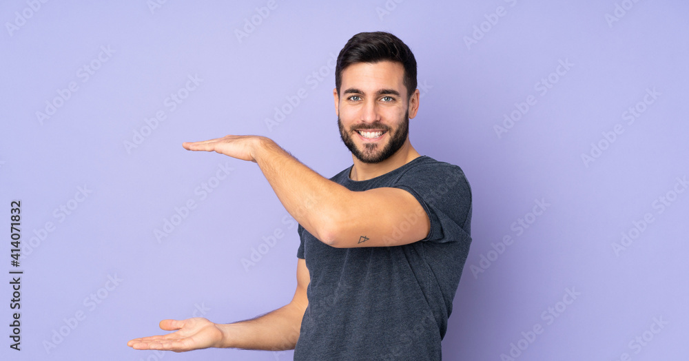 Caucasian handsome man holding copyspace to insert an ad over isolated purple background Caucasian handsome man holding copyspace to insert an ad over isolated purple background