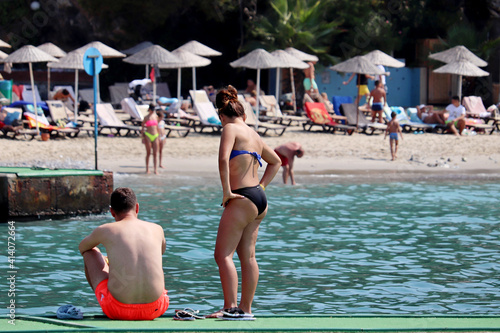 Fototapeta Naklejka Na Ścianę i Meble -  Couple on a pier on sea beach and sunbathing people on background. Man and woman in bikini together, family holiday on resort