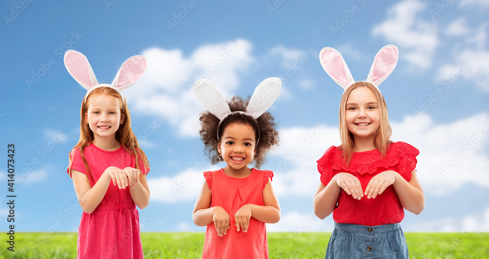 easter, holidays and childhood concept - group of happy smiling girls wearing bunny ears headbands over blue sky and grass background easter, holidays and childhood concept - group of happy smiling girls wearing bunny ears headbands over blue sky and grass background
