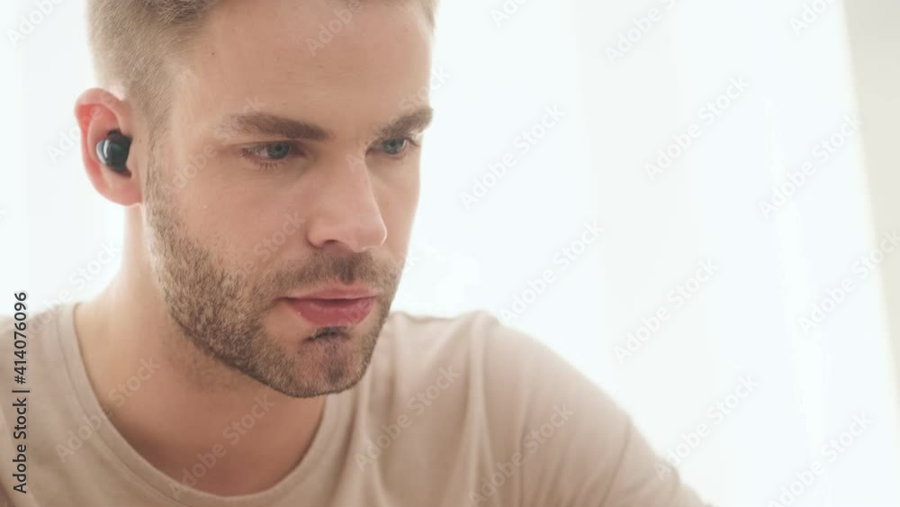 A focused young man wearing earbuds is eating breakfast in the kitchen at home A focused young man wearing earbuds is eating breakfast in the kitchen at home