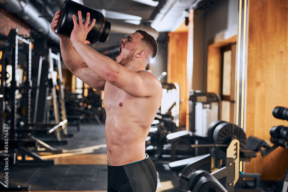 Naklejka premium Young handsome bodybuilder having supplements during workout