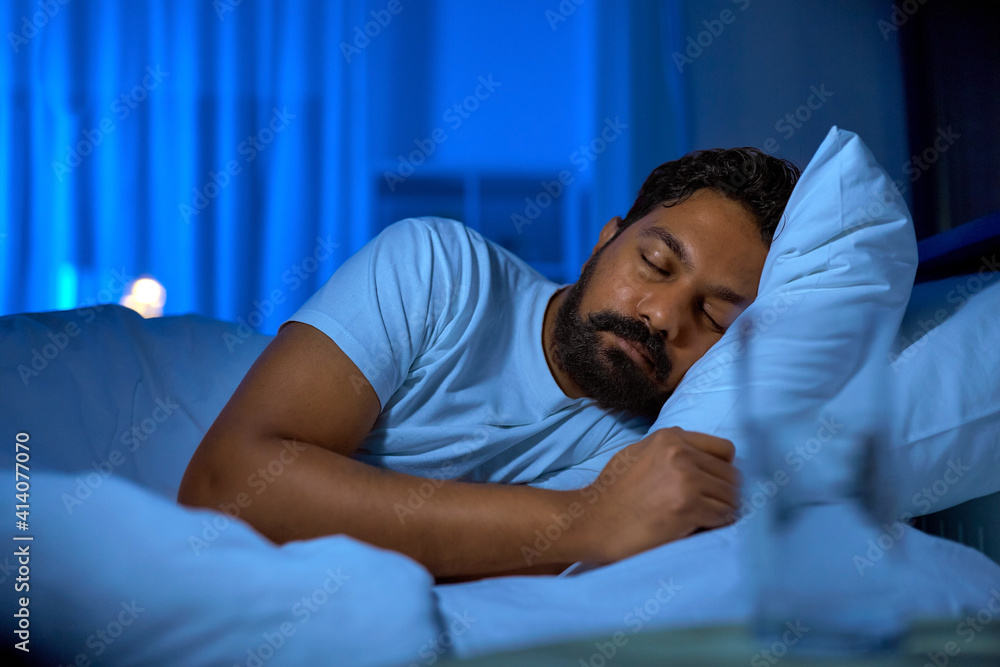 people, bedtime and rest concept - indian man sleeping in bed at home at night